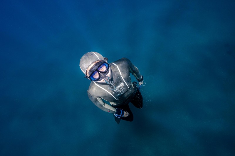 Freediver exhaling small bubbles while descending toward a reef